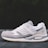 A white and gray athletic shoe with a modern design is positioned on a flat surface against a blurred dark background. The shoe features a mix of materials, including mesh and suede, and showcases detailed stitching with a visible logo and embossed text on the side.