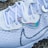 A close-up of a stylish white athletic shoe with intricate patterns and shoelaces. The shoe features a sleek design with iridescent accents near the eyelets and on a prominent logo.