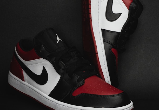 A pair of stylish athletic shoes in black, white, and red colors with distinctive branding. The shoes are positioned against a dark background, showcasing their sleek design and detailed craftsmanship.