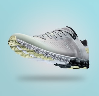 A single sports shoe is prominently displayed against a seamless, light turquoise background. The shoe features a sleek design with a gradient of light gray to dark gray tones, and is equipped with a distinctive CloudTec sole for cushioning. The branding logo is subtly visible on the side.