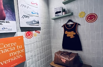 A small retro-themed display with a focus on athletic apparel and shoes. The walls feature a series of posters showcasing various Nike shoes from different years. A black gym tank top and a brown leather gym bag are prominently positioned on a wooden bench. There are decorative elements like potted plants on wall-mounted shelves and smiley face icons. The environment has a nostalgic and sporty atmosphere.