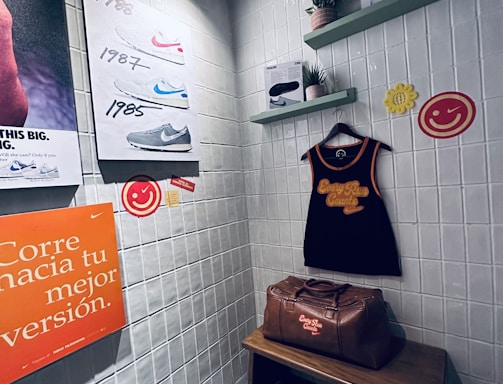 A small retro-themed display with a focus on athletic apparel and shoes. The walls feature a series of posters showcasing various Nike shoes from different years. A black gym tank top and a brown leather gym bag are prominently positioned on a wooden bench. There are decorative elements like potted plants on wall-mounted shelves and smiley face icons. The environment has a nostalgic and sporty atmosphere.
